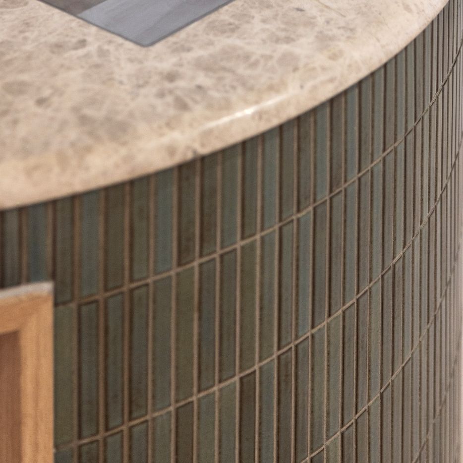 Close-up of a curved reception desk with green mosaic tiles and a polished stone countertop – modern office interior design.
