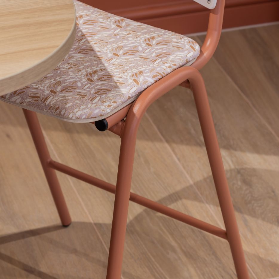 Modern cafe chair with a terracotta metal frame and patterned upholstered seat, paired with a round wooden table on light timber flooring.